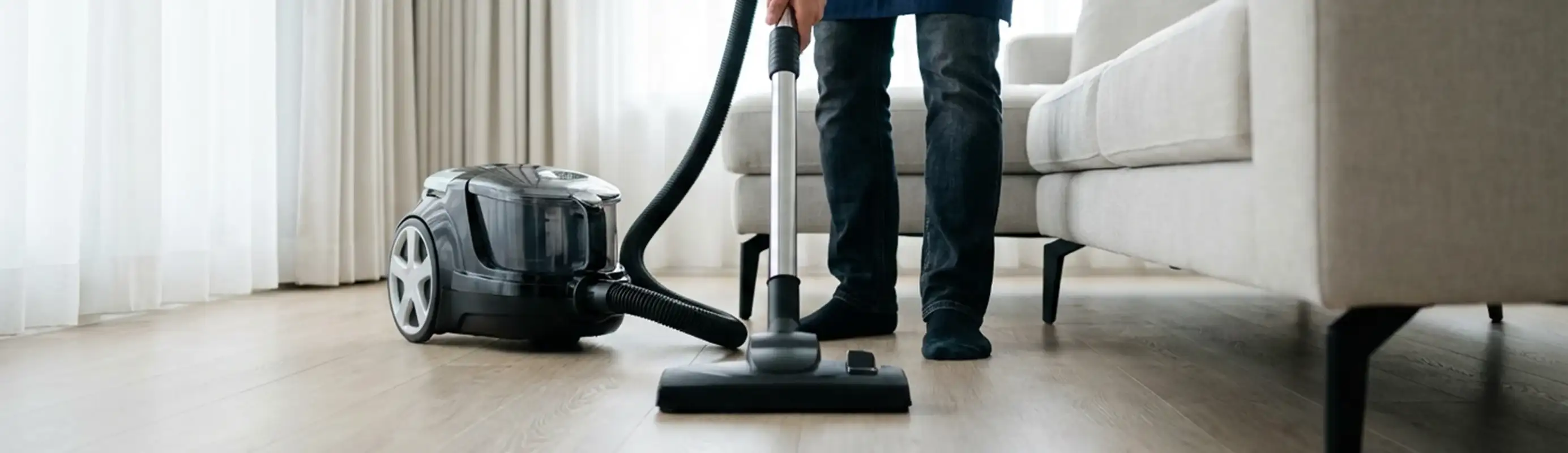 Professional house cleaner vacuuming a living room floor with a canister vacuum cleaner, Cincinnati, OH.