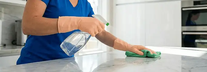 Maid service worker spraying and wiping a kitchen countertop with a microfiber cloth for sanitizing, Cincinnati, OH.