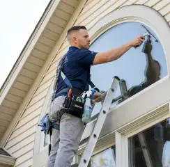Professional window cleaner on a ladder using a squeegee to clean an exterior arched window, Cincinnati, OH.