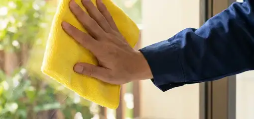 House cleaner wiping a glass window with a yellow microfiber cloth for streak-free cleaning, Cincinnati, OH.